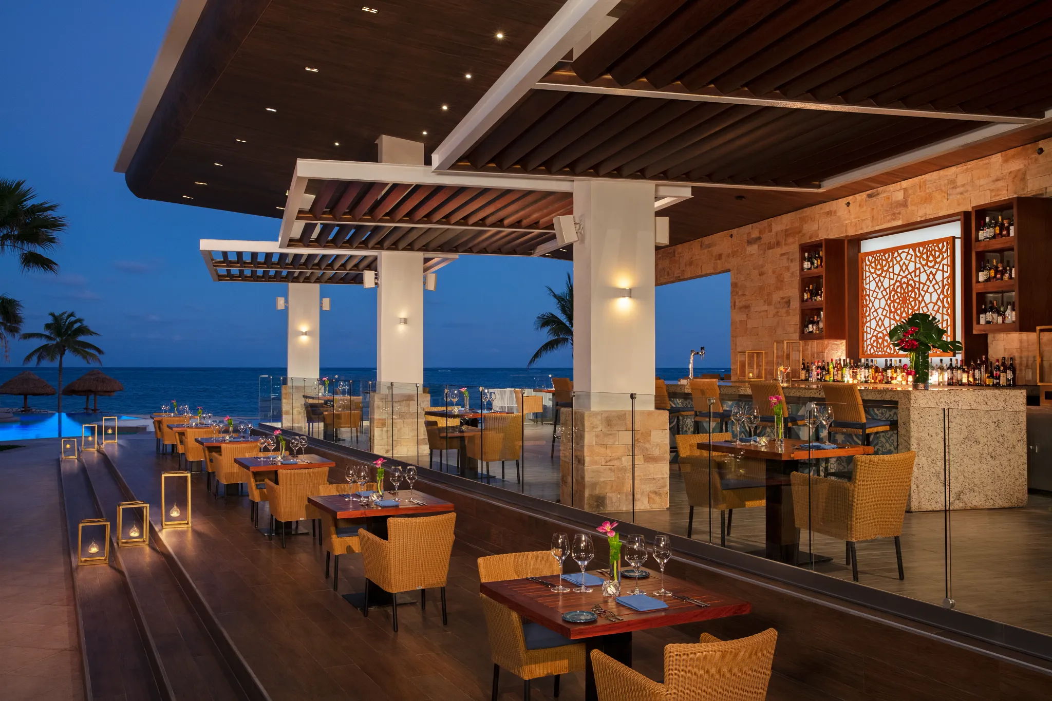 Rosewater restaurant at Secrets Riviera Cancun featuring open-air oceanfront dining, elegant table settings, and a stylish bar terrace at sunset.